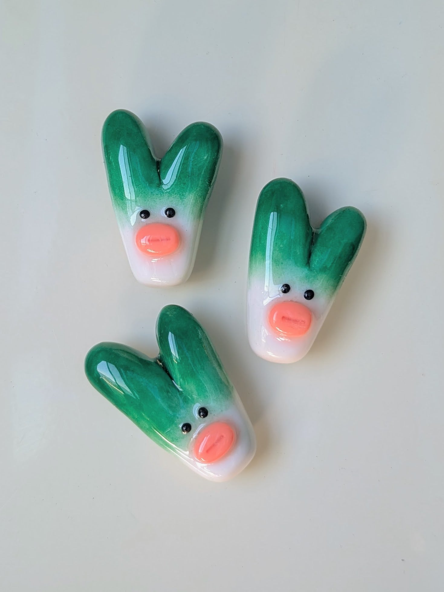 Three green onion clay magnets with pink lips on a white background