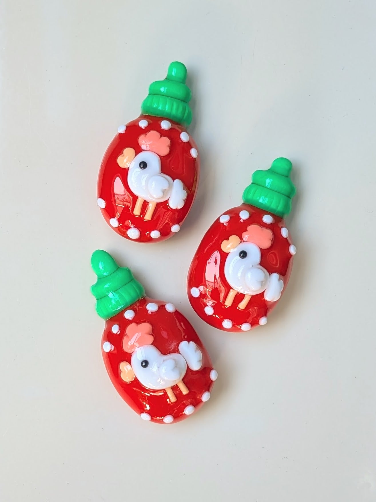 Three red sriracha bottle magnets with cartoon chicken design on a white background